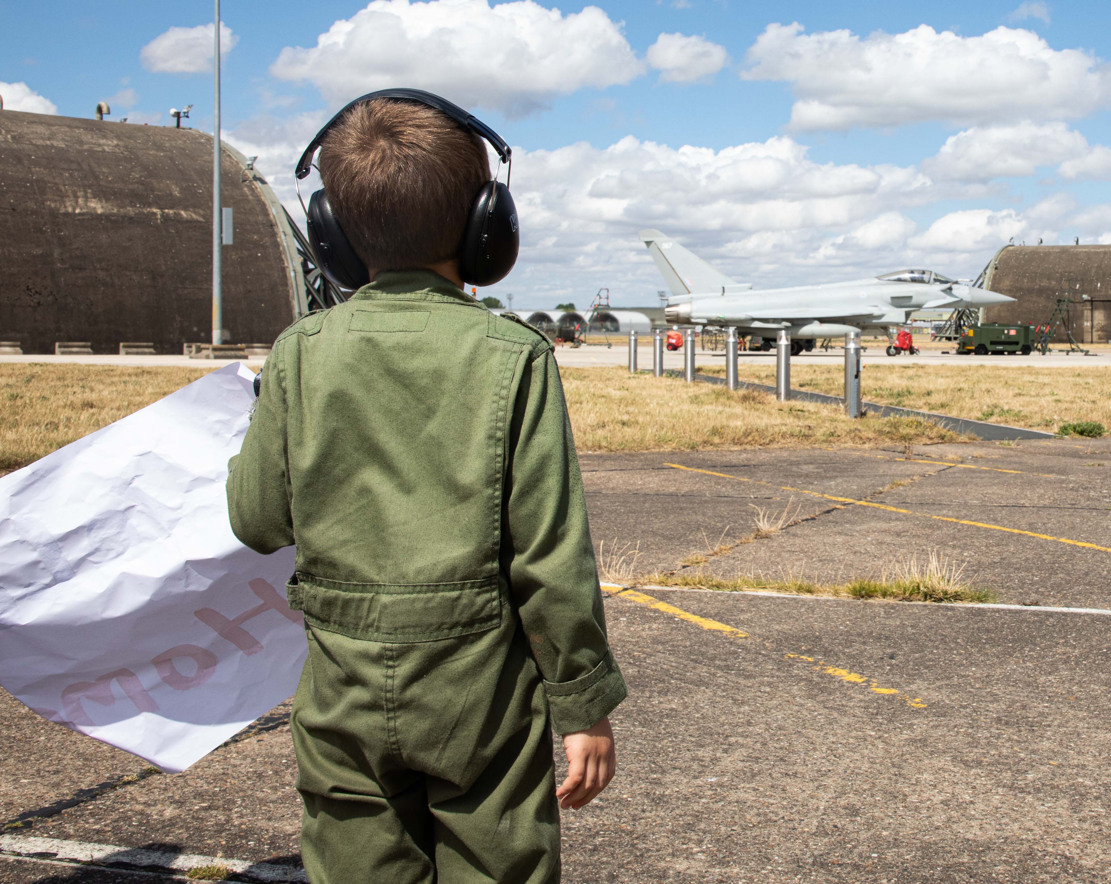 Image shows young boy holding a poster on the airfield.